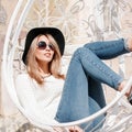 European stylish young woman hipster in sunglasses in a luxurious hat in stylish jeans in a knitted sweater in sneakers lies Royalty Free Stock Photo