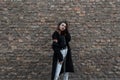 European stylish young woman in a vintage black long coat in white jeans in a fashionable t-shirt posing standing Royalty Free Stock Photo