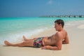 European tanned handsome man wearing swimming shorts at tropical sandy beach at island luxury resort Royalty Free Stock Photo
