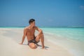 European tanned man wearing swimming shorts sitting at tropical sandy beach at island luxury resort Royalty Free Stock Photo