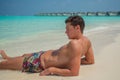 European tanned man wearing swimming shorts at tropical sandy beach at island luxury resort Royalty Free Stock Photo