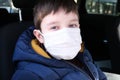 A european teen caucasian boy in car wearing white surgical medical face mask as a protection against virus disease