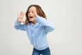 European teenager girl in a blue hoodie shouts the news while holding hands at the mouth on a light background