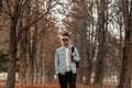 European trendy handsome young man in stylish jeans clothes in vintage sunglasses with a fashionable hairstyle with backpack walks Royalty Free Stock Photo
