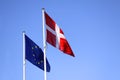 European Union EU and danish flag for Denmark on a pole waving in the wind with a blue sky on a sunny day