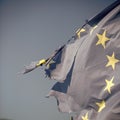 European union twelve star flag torn and with knots in wind on blue sky background, close up. Flag is torn off at side