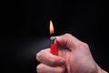 mans hand holds a burning red ignited plastic gas lighter with fire on an isolated black background Royalty Free Stock Photo