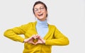 European woman making heart shape with fingers. Beautiful female smile broadly in blue and yellow sweater showing heart gesture