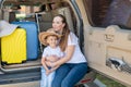 European woman sitting with her son in the trunk of an SUV. Beautiful happy mother loving hugs son. Yellow luggage for Royalty Free Stock Photo