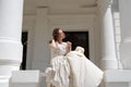 European woman sitting in sunshine and touching hair in vintage dress near palace.