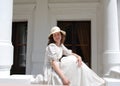 European woman sitting in sunshine and touching hair in vintage dress near palace.