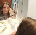 European woman tweeze eyebrows at bathroom