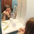 European woman tweeze eyebrows at bathroom