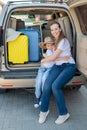 European woman sitting with her son in the trunk of an SUV. Beautiful happy mother loving hugs son. Yellow luggage for Royalty Free Stock Photo