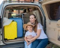 European woman sitting with her son in the trunk of an SUV. Beautiful happy mother loving hugs son. Yellow luggage for Royalty Free Stock Photo