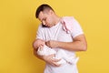 European young father busy with phone conversation, posing with his newborn baby isolated over yellow background, handsome daddy