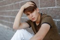 European young man in a fashionable green T-shirt in stylish white pants with a fashionable hairstyle relaxes sitting