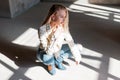 European young woman model in vintage leather jacket in blue trendy ripped jeans in green fashionable cowboy boots posing sitting Royalty Free Stock Photo