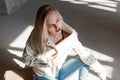 European young woman in vintage leather jacket in fashionable ripped jeans in blue trendy cowboy boots posing sitting indoors Royalty Free Stock Photo