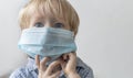 Europeanan Caucasian boy child kid toddler blond in blue medical mask on gray background. Concept of epidemic virus
