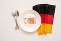 10 euros lie on a plate next to a spoon and a fork and the flag of Germany on a white background ,finance and economy of Royalty Free Stock Photo