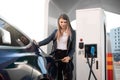 EV charging station, eco fuel concept. Portrait of pretty young girl inserting charging plug into her modern electric