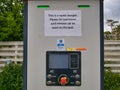 An EV electric vehicle rapid charger with a sign asking customers to be courteous and to move their car when charged.