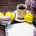 An even row of multicolored macaroons, a small alarm clock, a cup of coffee and a notebook on a wooden background. Royalty Free Stock Photo