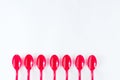 An even row of seven red plastic spoons down below on white background with empty space for text.