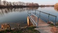 Evenig view of concrete molo on dam of large artigicial fish pond with spillway channel hatch and railing.