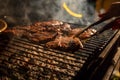 In the evening a barbecue grill on which tasty juicy steaks are grilled over an open fire, a hand holds tongs and turns