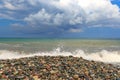 In the evening, a burst of waves on a pebble beach. Cloudy and dramatic sky before sunset. Nature concept, design for postcard.