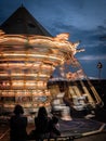 Carousel with many lights turns fast in front of steady spectators