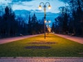 Evening city park. Wooden benches, street lights and park alley. The tiled road in the night park with lanterns. Benches in the Royalty Free Stock Photo