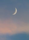 Crescent moon in a blue sky with pale pink clouds