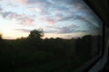 An evening landscape with a setting sun and beautiful clouds is seen through a large train window