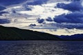 Evening landscape after the storm - dark blue sea, hilly coast, dark clouds on the sky illuminated by setting sun. Royalty Free Stock Photo