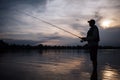 It is evening outside. Fisherman stands in shallow and fishing. He holds fly rod in hands. There is a reel under it. He Royalty Free Stock Photo