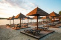 Evening sandy beach with brown wooden loungers and umbrellas Royalty Free Stock Photo