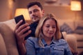 Evening Shot Of Couple Relaxing On Sofa At Home As Man Looks At Mobile Phone And Woman Reads Book Royalty Free Stock Photo