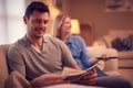 Evening Shot Of Couple Relaxing On Sofa At Home As Man Reads Book And Woman Watches TV Royalty Free Stock Photo