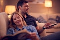 Evening Shot Of Couple Relaxing On Sofa At Home As Woman Reads Book And Man Watches TV Royalty Free Stock Photo
