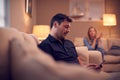 Evening Shot Of Couple On Sofa At Home With Man Looking At Mobile Phone And Unhappy Woman Behind Royalty Free Stock Photo