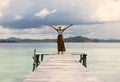 An evening shot of a tourist woman standing with oper arms, hat, at the end of a pier looking in the water and at the sunset Royalty Free Stock Photo