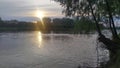 In the evening, the sun has lowered to the horizon and its rays break through the clouds above the trees on the opposite bank of t Royalty Free Stock Photo