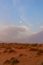 Evening sunset in the desert sand dunes of the United Arab Emirates with a blue sky, clouds, and the moon shining brightly with Royalty Free Stock Photo