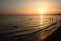 In the evening at sunset, several people are in the sea and bathe in front of a red and glowing background Royalty Free Stock Photo