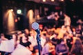 Event hall: Close up of microphone stand, seats with audience in the blurry background Royalty Free Stock Photo
