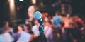 Event hall: Close up of microphone stand, seats with audience in the blurry background Royalty Free Stock Photo