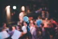 Event hall: Close up of microphone stand, seats with audience in the blurry background Royalty Free Stock Photo